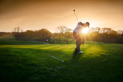 man playing golf with sun setting